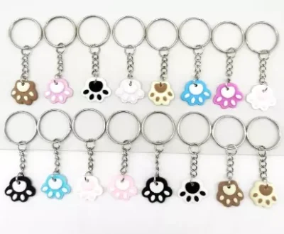 Set de 16 llaveros metálicos con colgantes de huellita de perro o gato en variados colores sobre fondo blanco.